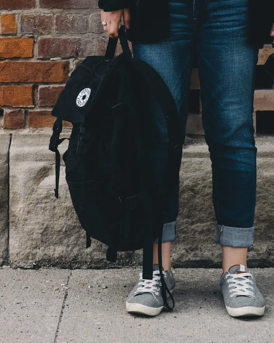 Person standing on the sidewalk holding a backpack